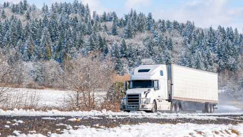 Truck and trailer driving through a snowy landscape.