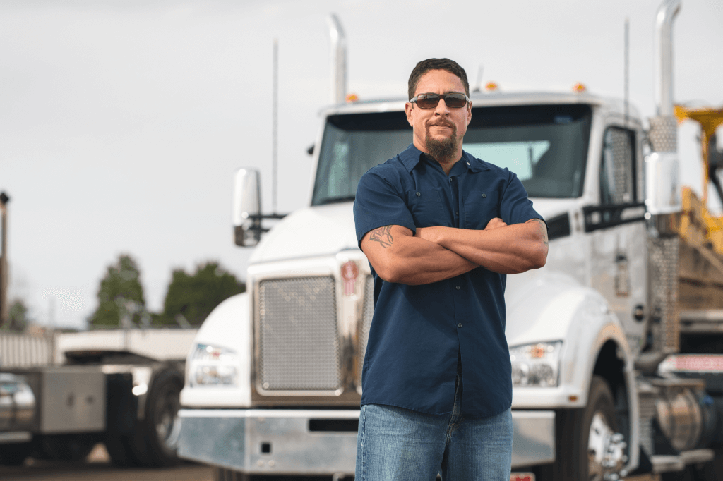 Person with crossed arms stands with truck in the background.