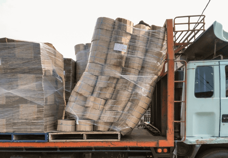 Wrapped pallet of cargo leaning against the cab protector of a flatbed trailer.