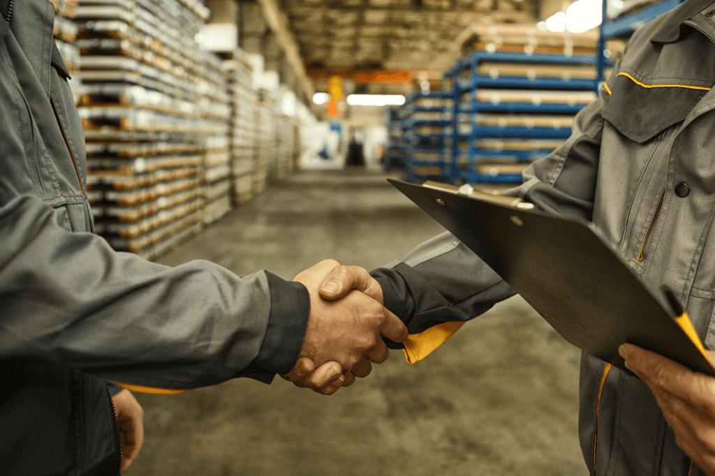 Two people shaking hands in a room with stacked pallets