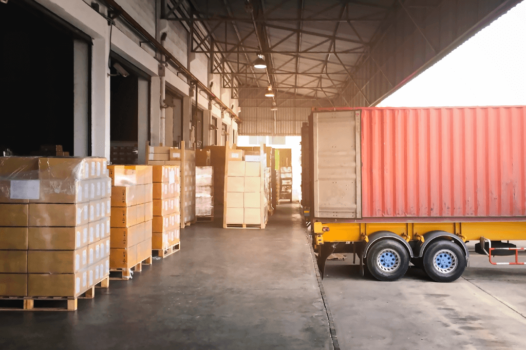 loading dock laden with pallets of boxes with a trailer backed up with doors open.