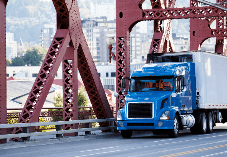 Truck and trailer crossing a bridge with a city in the background.