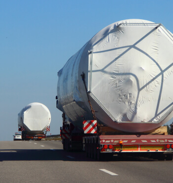 Two heavy haulers carrying large heavy cylinders driving down a freeway.