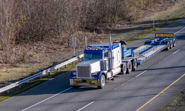 A blue tractor pulls an empty low boy trailer