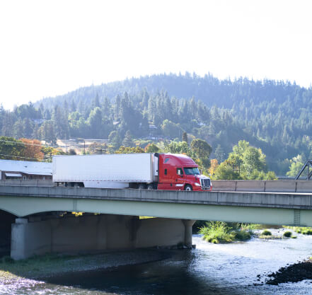 Red tractor with refer trailer crossing a bridge in the mountains.